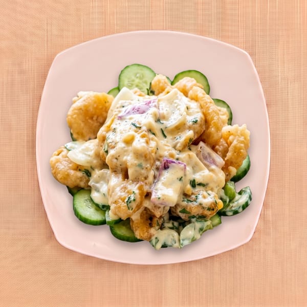 Crispy golden fritters topped with creamy herb sauce, red onion, and cucumber slices on a pink plate.
