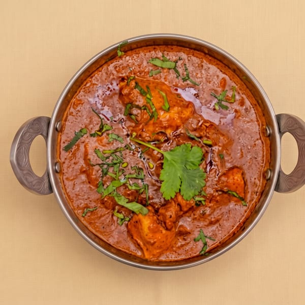 Creamy orange Indian curry garnished with cilantro, served in a handled metal bowl.