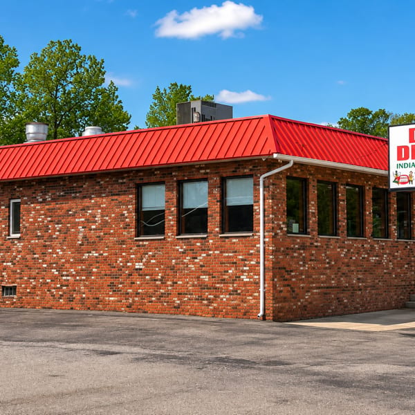 Exterior of Desi Dhaba Indian Restaurant, a brick building with a bright red roof and roadside sign.