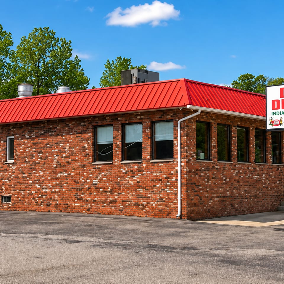 Exterior of Desi Dhaba Indian Restaurant, a brick building with a bright red roof and roadside sign.