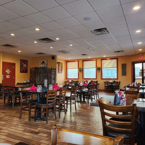 Spacious restaurant dining room with wooden tables, colorful napkins, tiled floors, decorative screens, and warmly lit yellow walls.