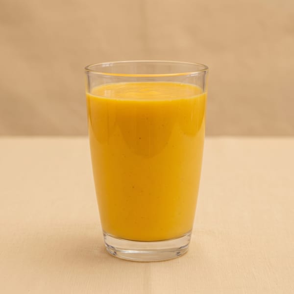 A clear glass filled with bright orange juice sits on a beige tabletop against a warm neutral background.