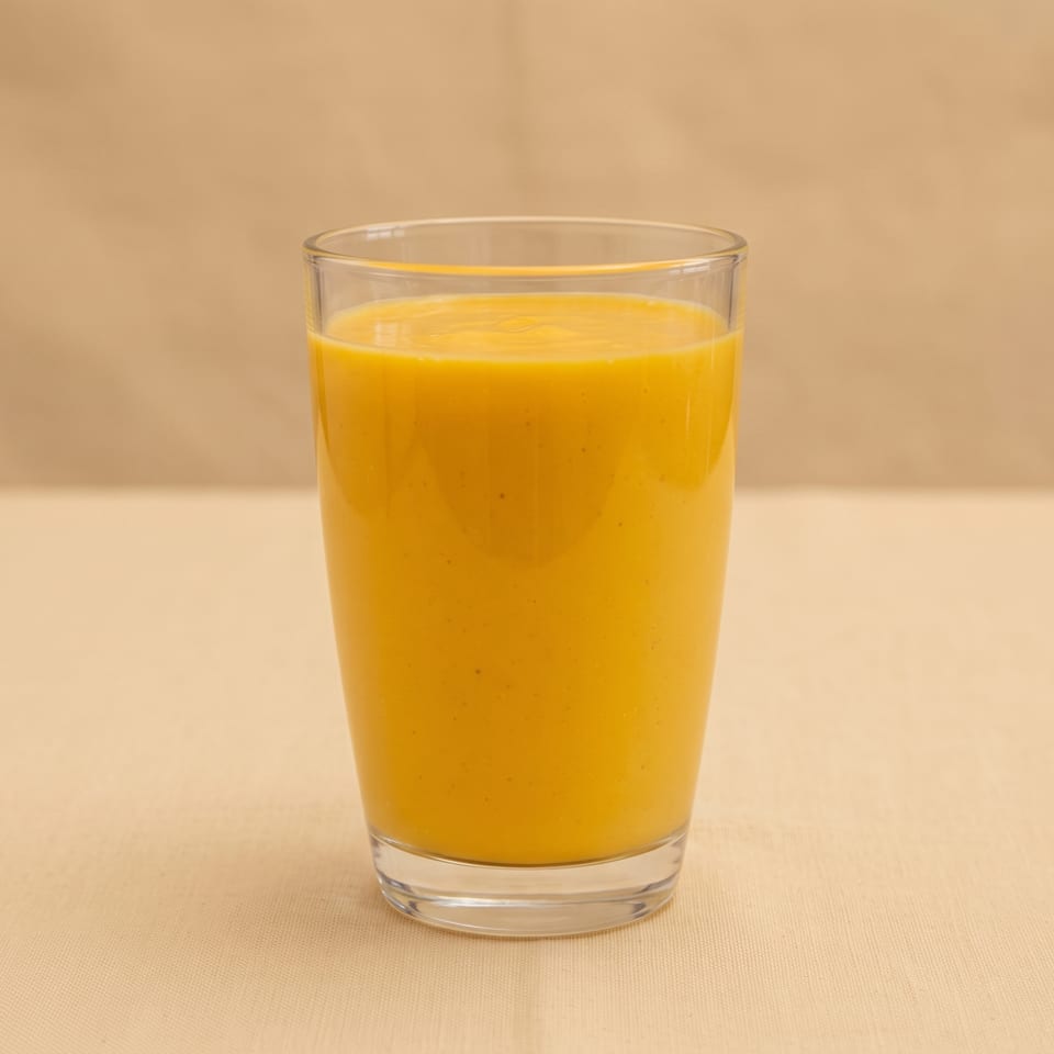 A clear glass filled with bright orange juice sits on a beige tabletop against a warm neutral background.