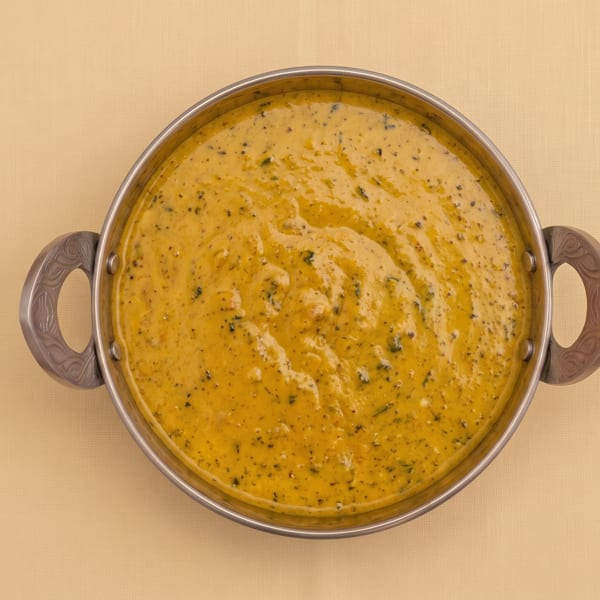 Top-down view of creamy golden curry speckled with herbs in a handled metal serving bowl.