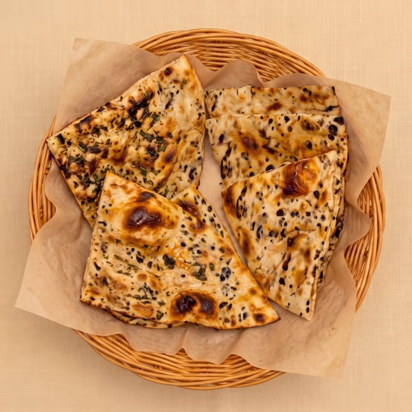 Basket of grilled, herb- and black-seed-topped flatbread pieces lined with parchment.
