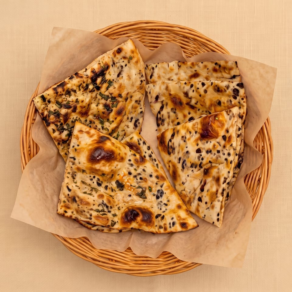Basket of grilled, herb- and black-seed-topped flatbread pieces lined with parchment.