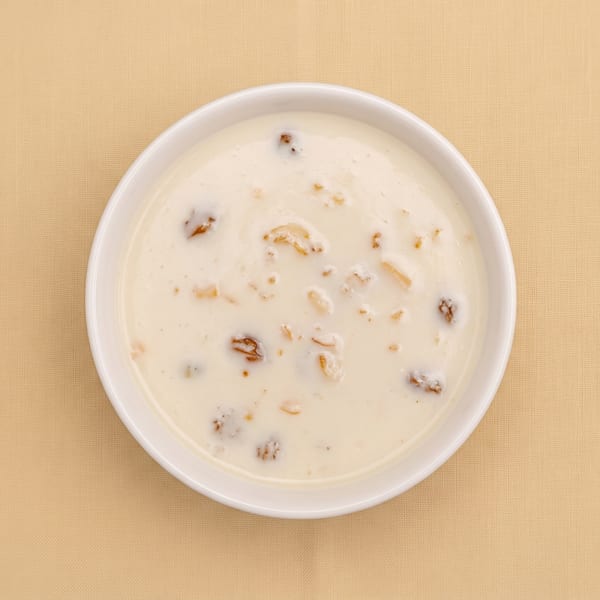 Overhead view of creamy dessert topped with raisins and chopped nuts in a white bowl on beige fabric.