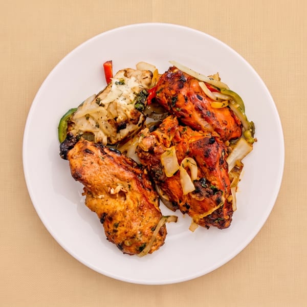 Plate of assorted grilled chicken pieces with charred edges, sautéed onions, and colorful bell peppers.