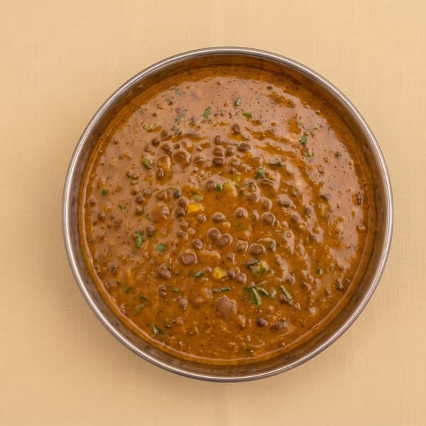 Overhead view of creamy Indian lentil curry garnished with herbs in a stainless steel bowl.